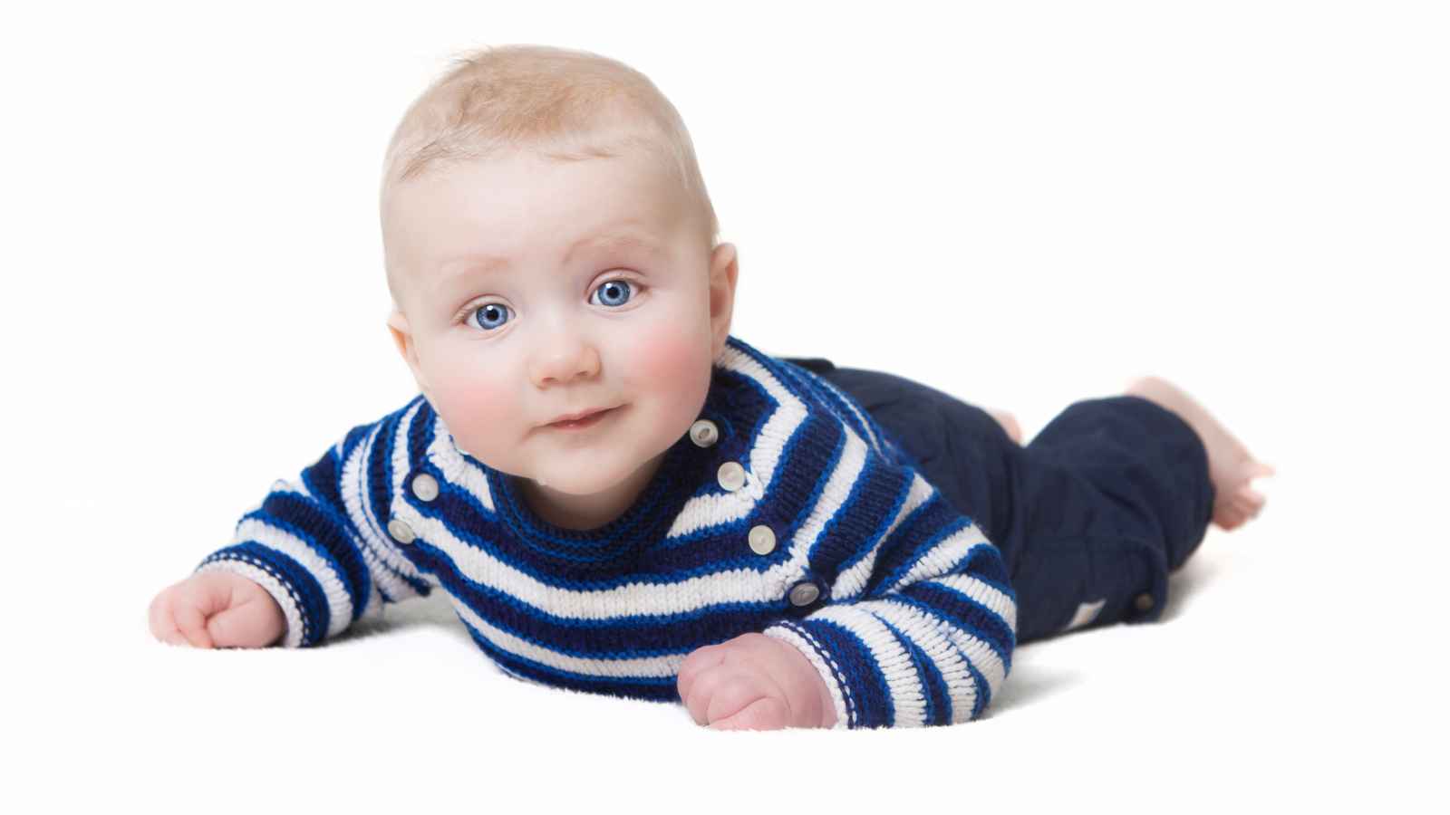 A baby boy crawling in a white surface wearing his white and blue knitted striped jacket and pants.