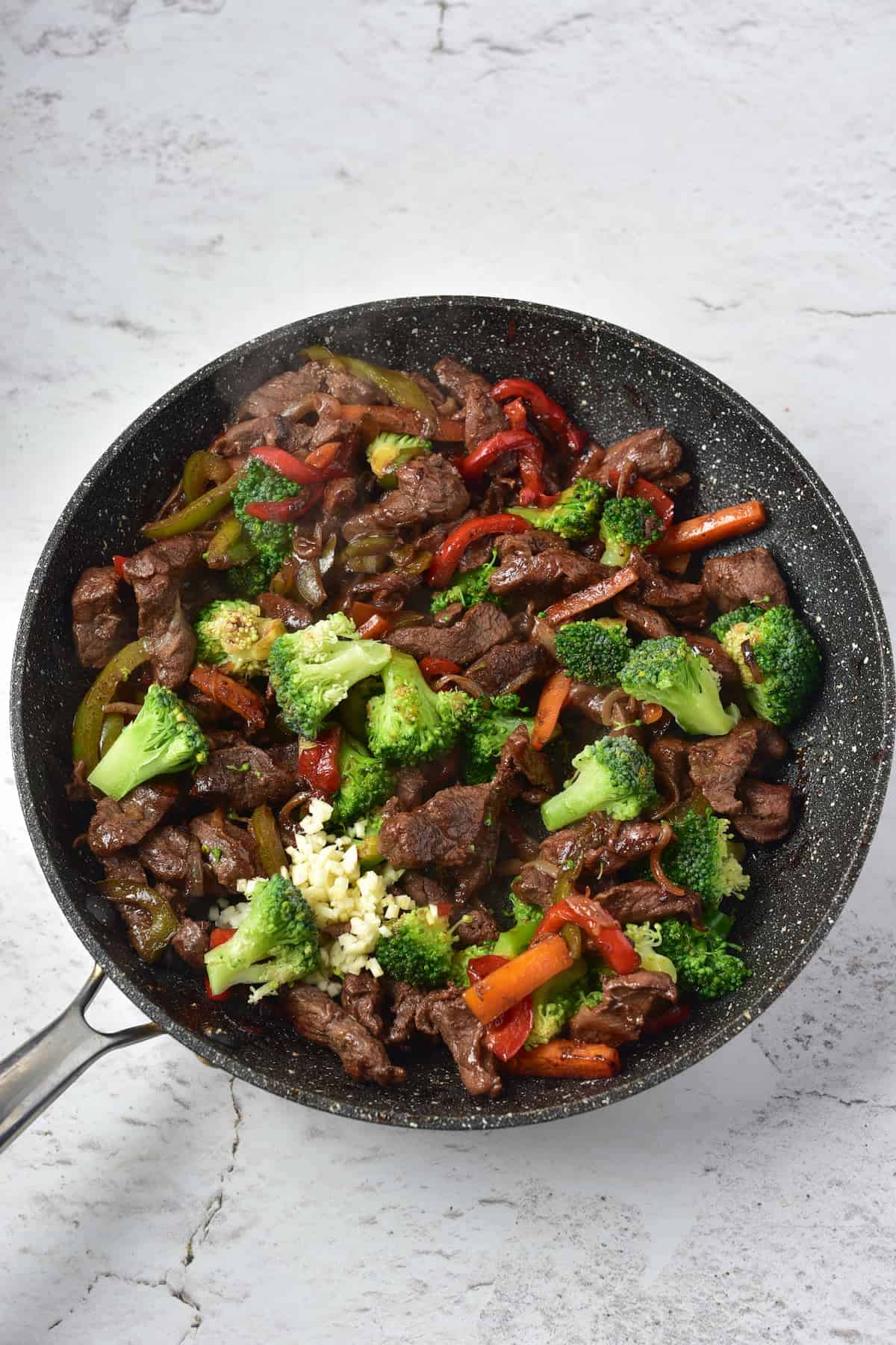 Cooked venison stir fry in a pan with some broccoli , set on a marble surface.