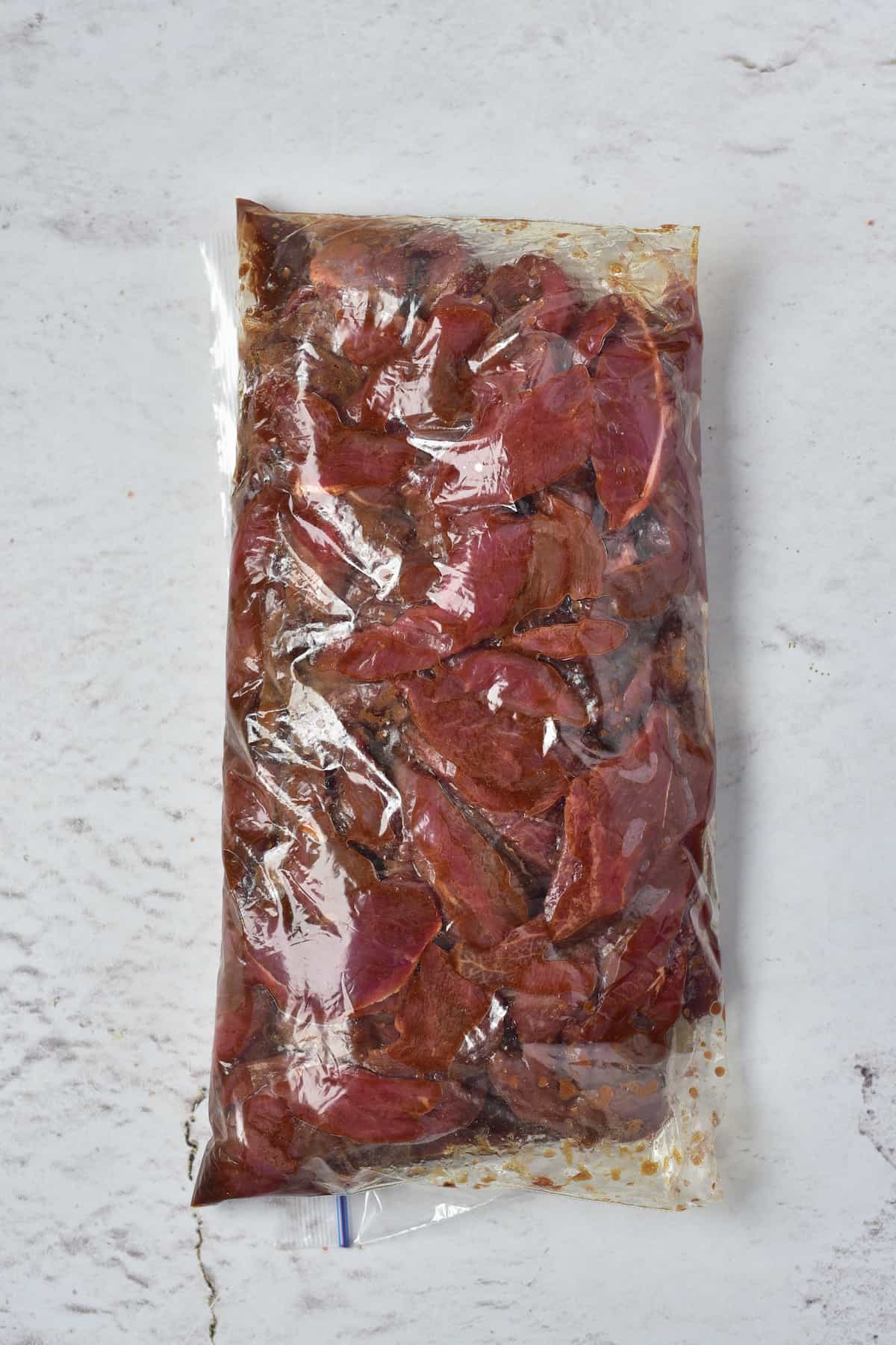 Marinated venison strips sealed in a plastic bag, ready for cooking.