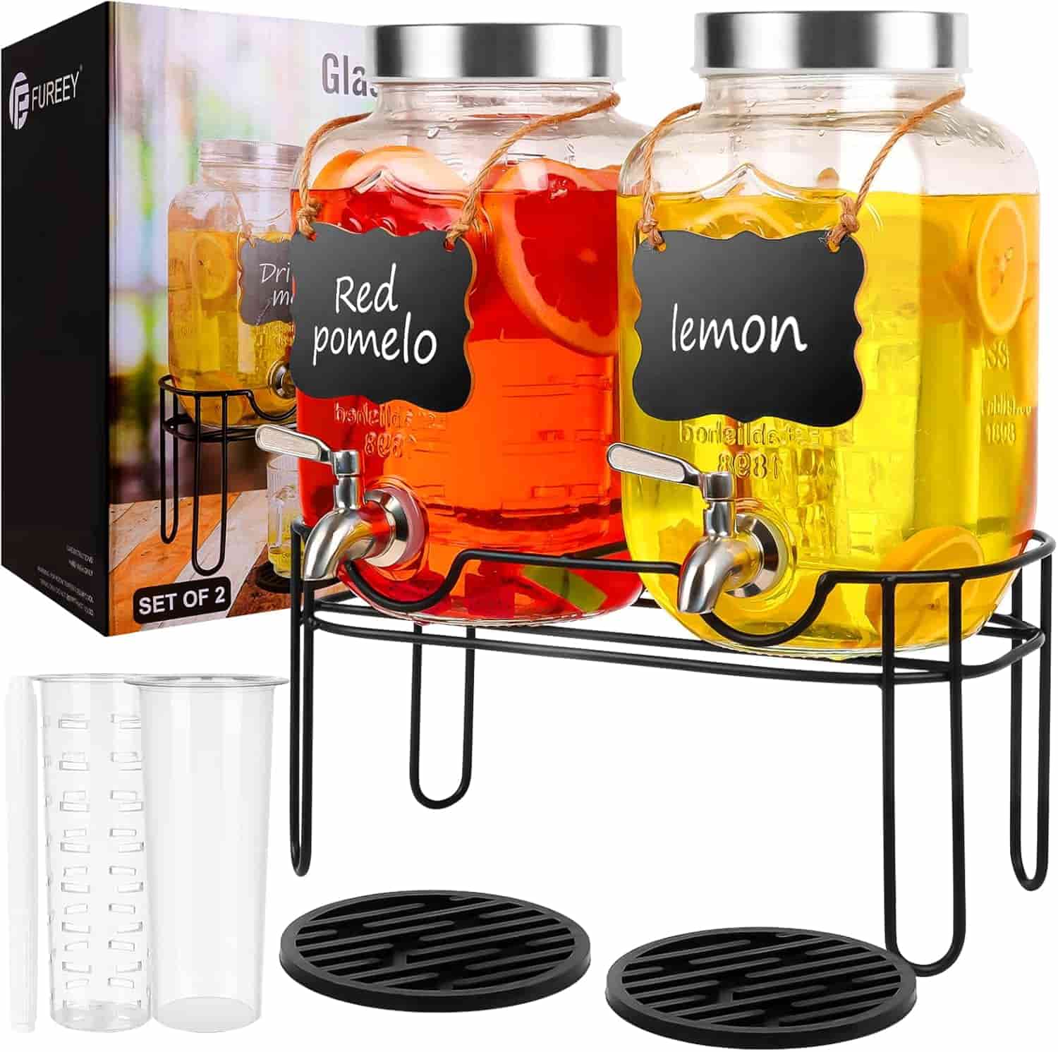 Two glass beverage dispensers labeled "Red pomelo" and "lemon" on a black stand, with lids, spigots, drip trays, a clear plastic measuring cup, and packaging in the background.