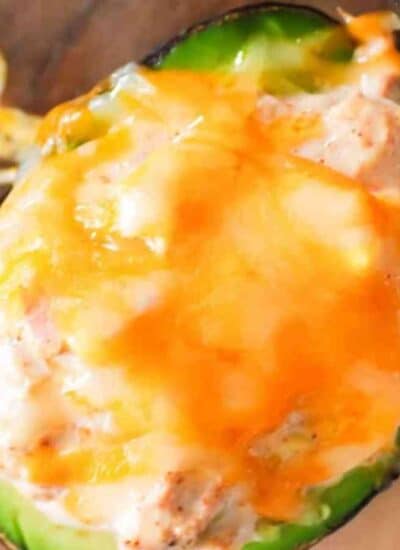 Halved avocado filled with a creamy mixture and topped with melted cheddar cheese, placed on a wooden surface.