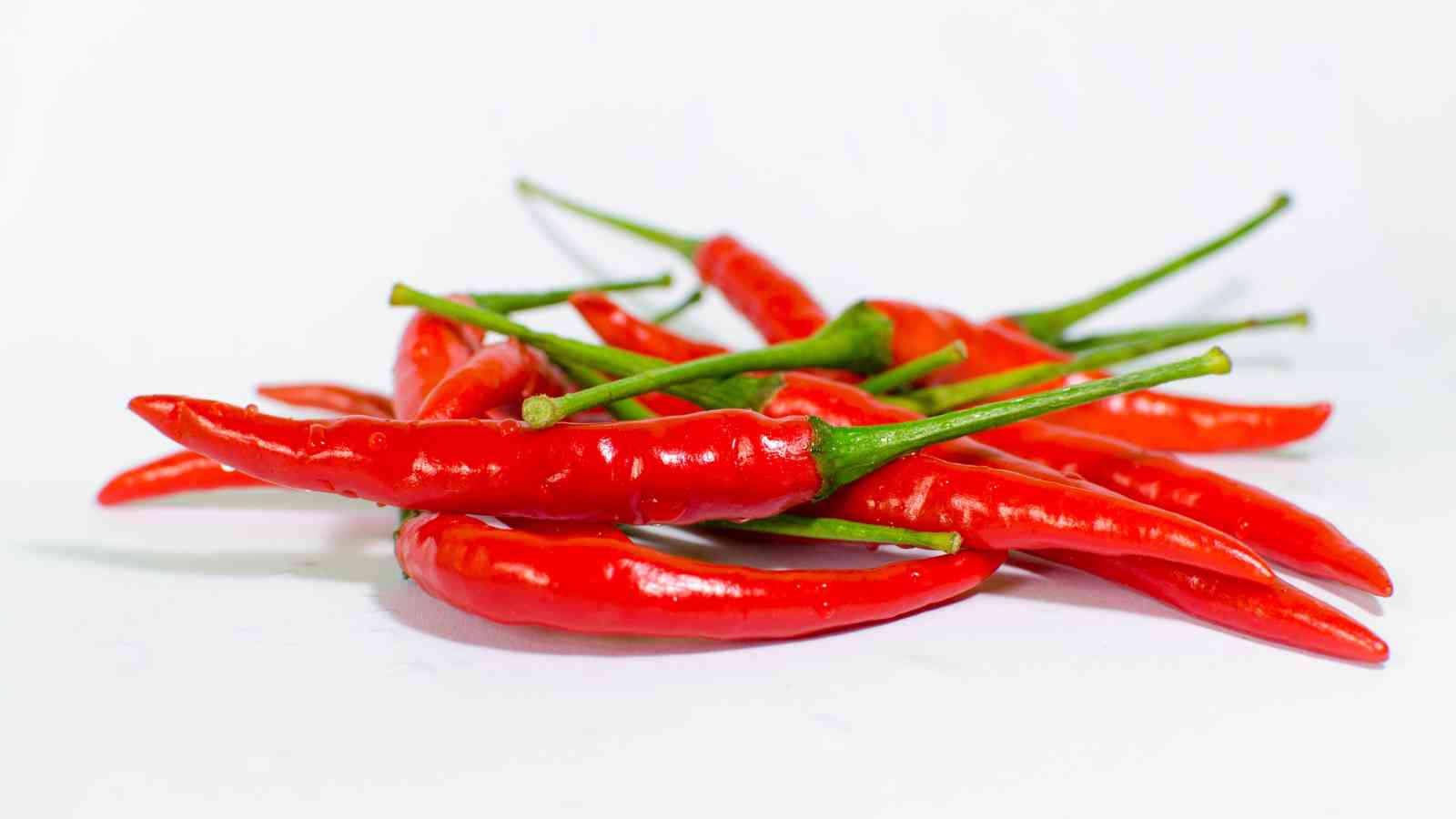 A pile of fresh red chili peppers with green stems is arranged on a white background.