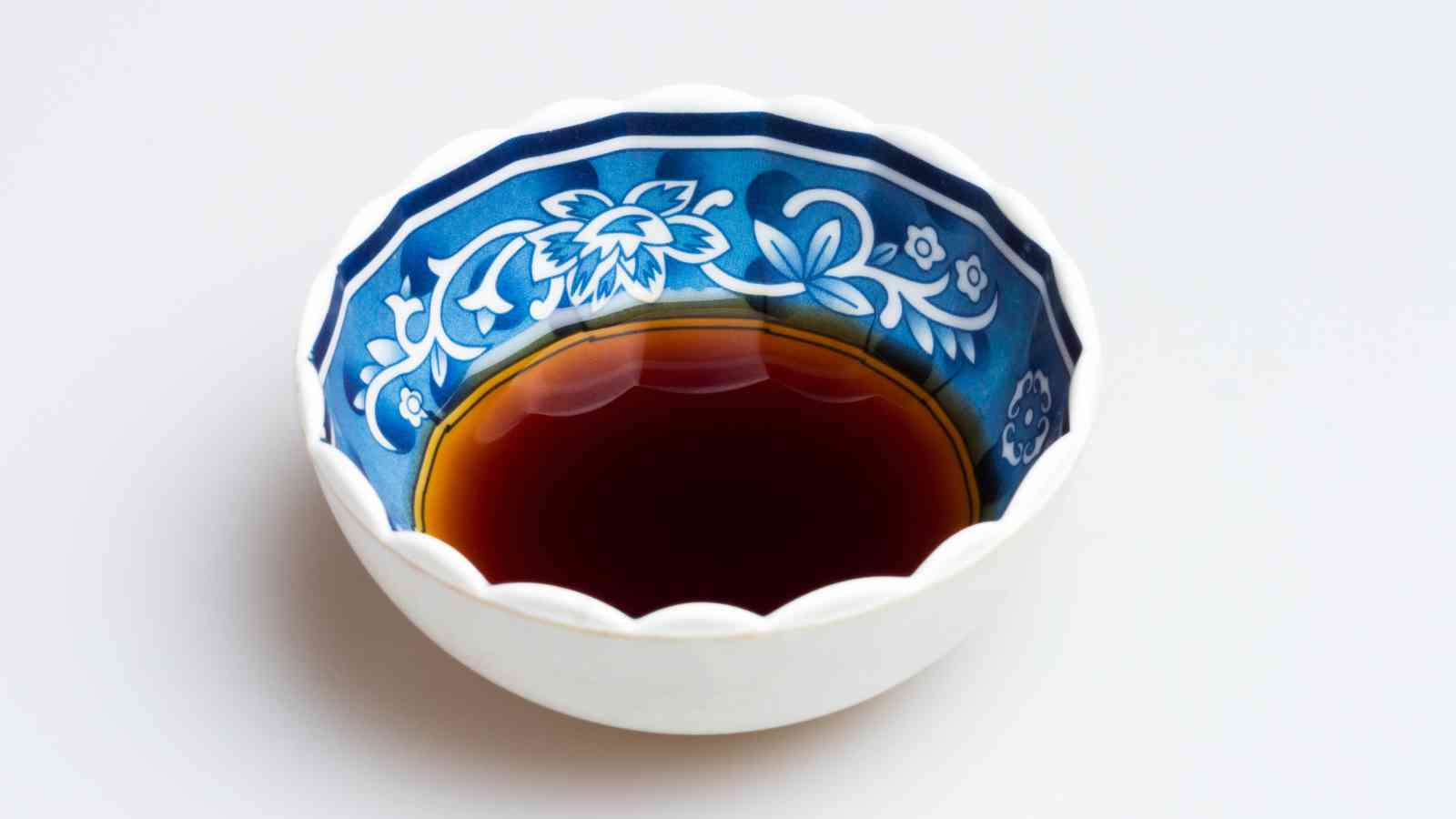 A small bowl with a blue and white floral pattern holds a black vinegar, against a plain white background.