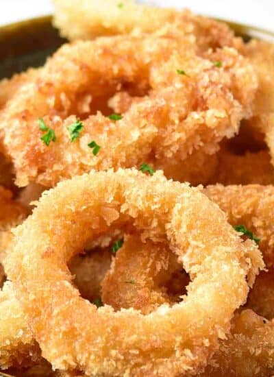 A bowl filled with golden, crispy fried calamari rings garnished with chopped parsley.