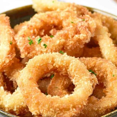 A bowl filled with golden, crispy fried calamari rings garnished with chopped parsley.