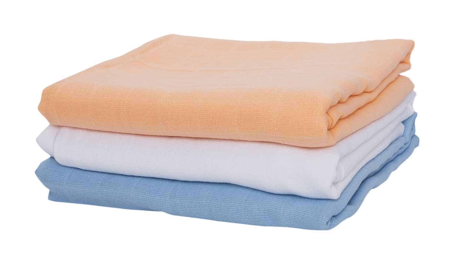 Three folded towels are stacked on top of each other: the top towel is peach, the middle is white, and the bottom is light blue, all on a white background.