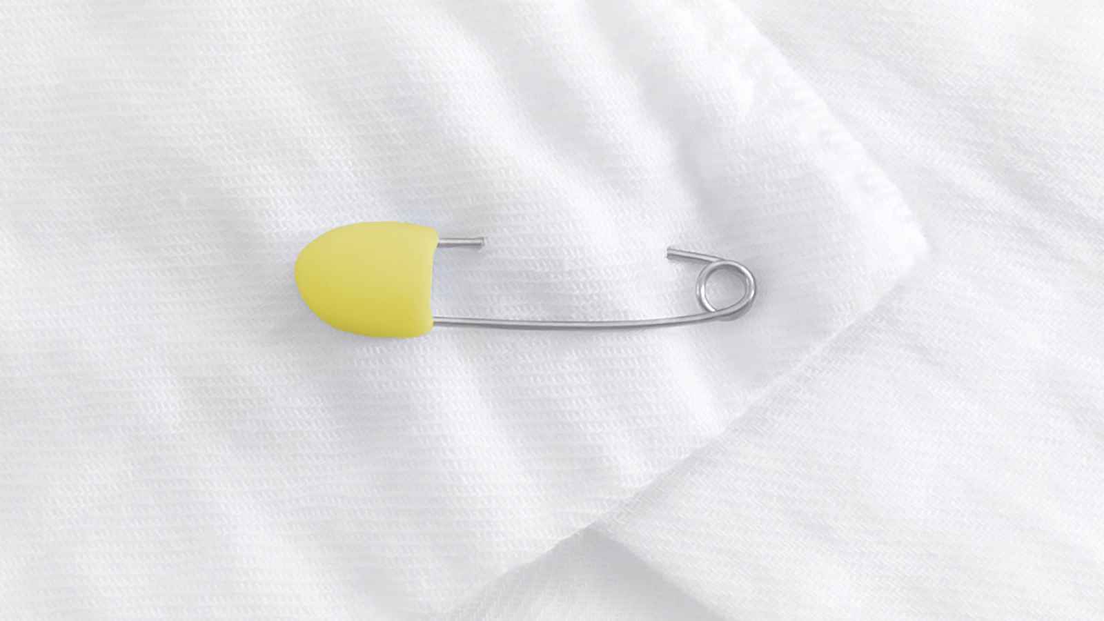 A silver safety pin with a yellow cap is placed on a white textured fabric surface.