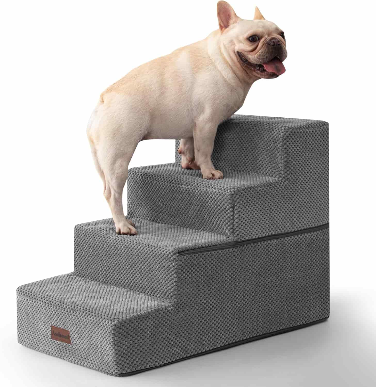 A light-colored French Bulldog stands on gray pet stairs with textured fabric and four steps.