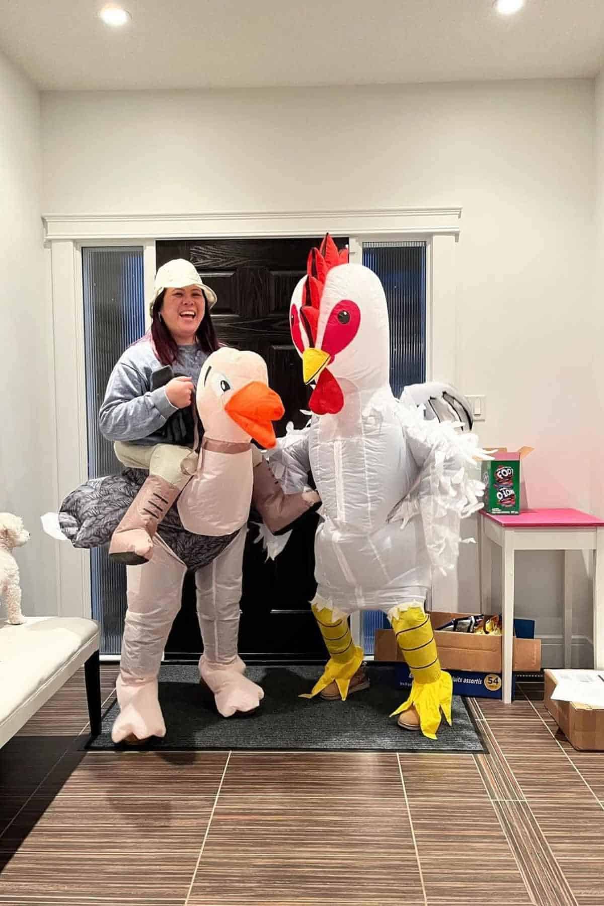 Two people in costume stand indoors; one wears a ride-on ostrich outfit, and the other wears an inflatable chicken suit.