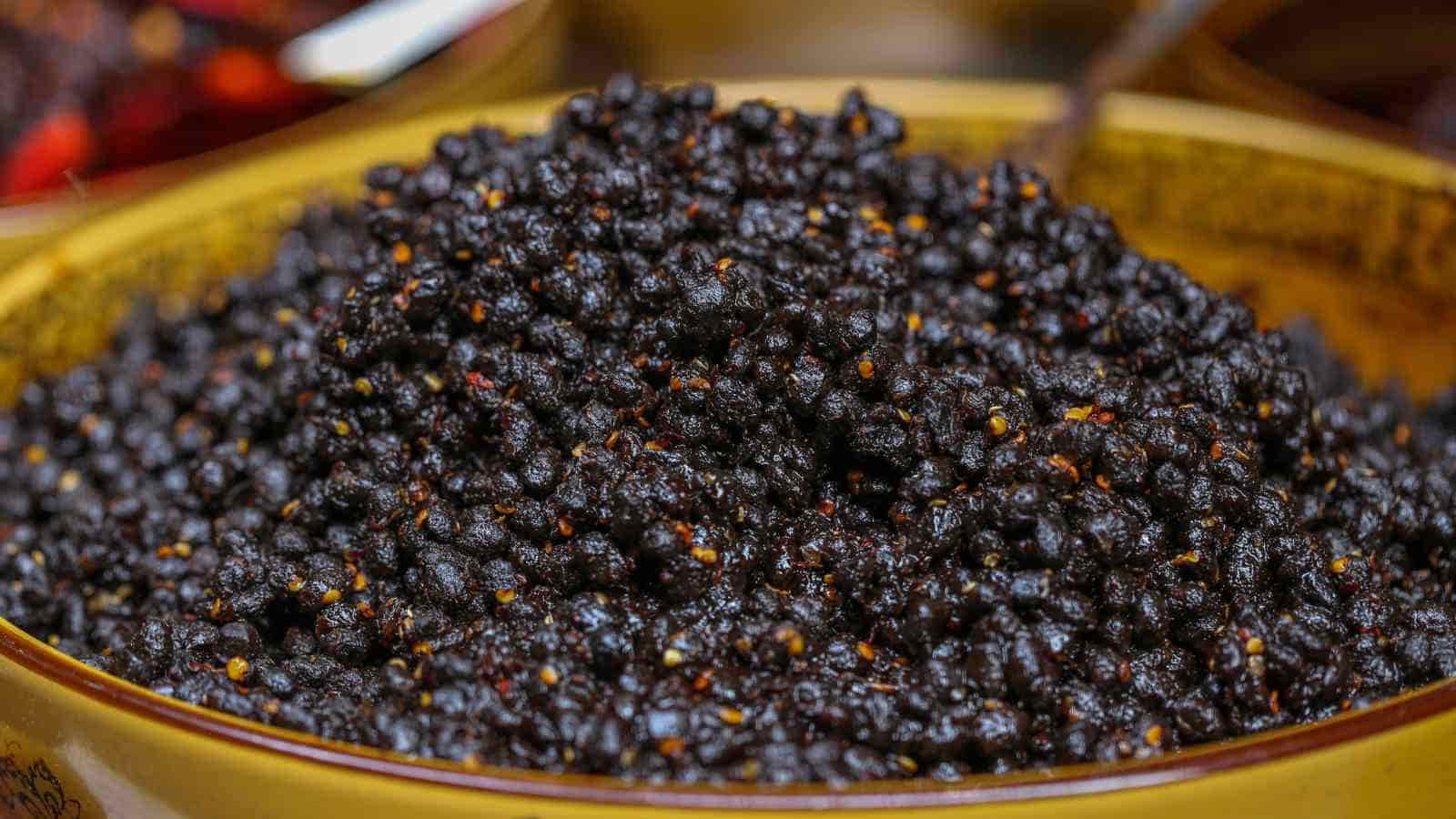A close-up of a bowl filled with dried black seeds, possibly elderberries or similar small, dark fruits.
