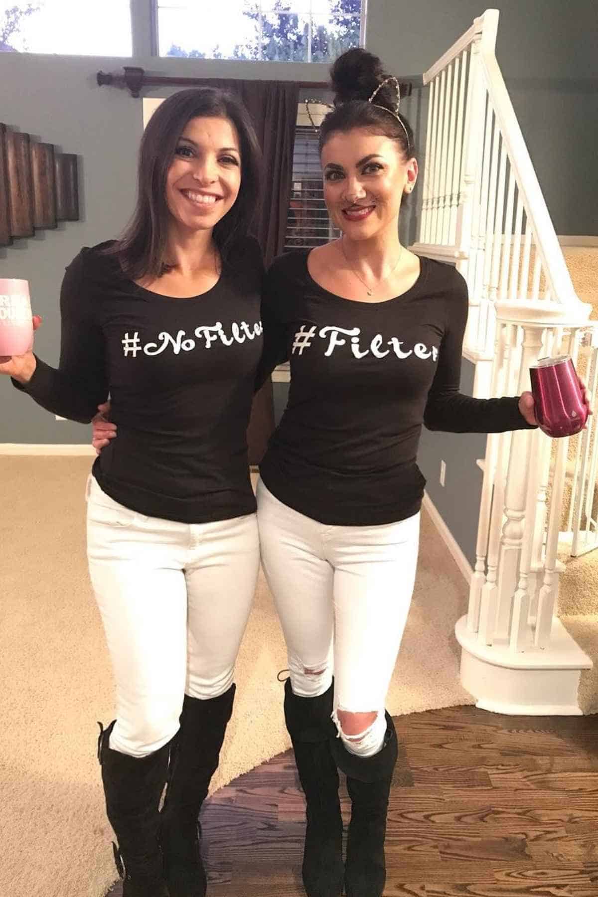 Two women stand indoors, smiling and holding mugs. One wears "#NoFilter" shirt and the other wears #Filter shirt. Both wears white pants, and black knee-high boots.