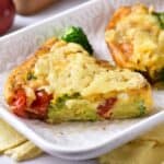 A slice of vegetable frittata with visible broccoli and tomatoes sits on a white plate.