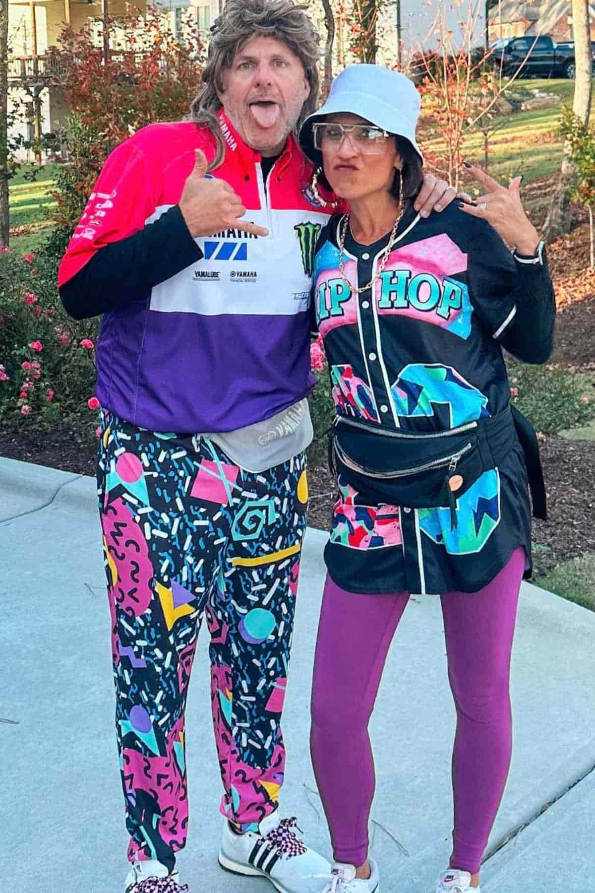Two adults pose outdoors in colorful, retro-themed outfits with bold patterns; one makes a funny face and the other gestures with hands, both dressed in 1980s or 1990s style clothing.