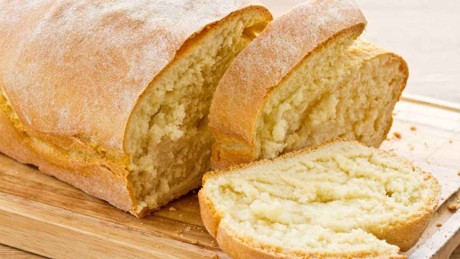 A loaf of homemade bread partially sliced on a wooden cutting board.