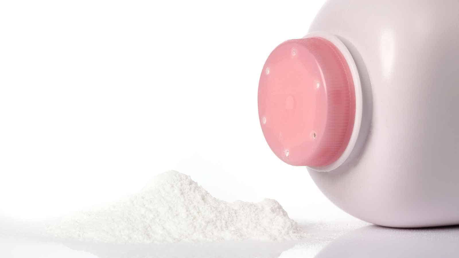 A white plastic bottle with a pink cap lies on its side, spilling a small mound of white powder onto a white surface.