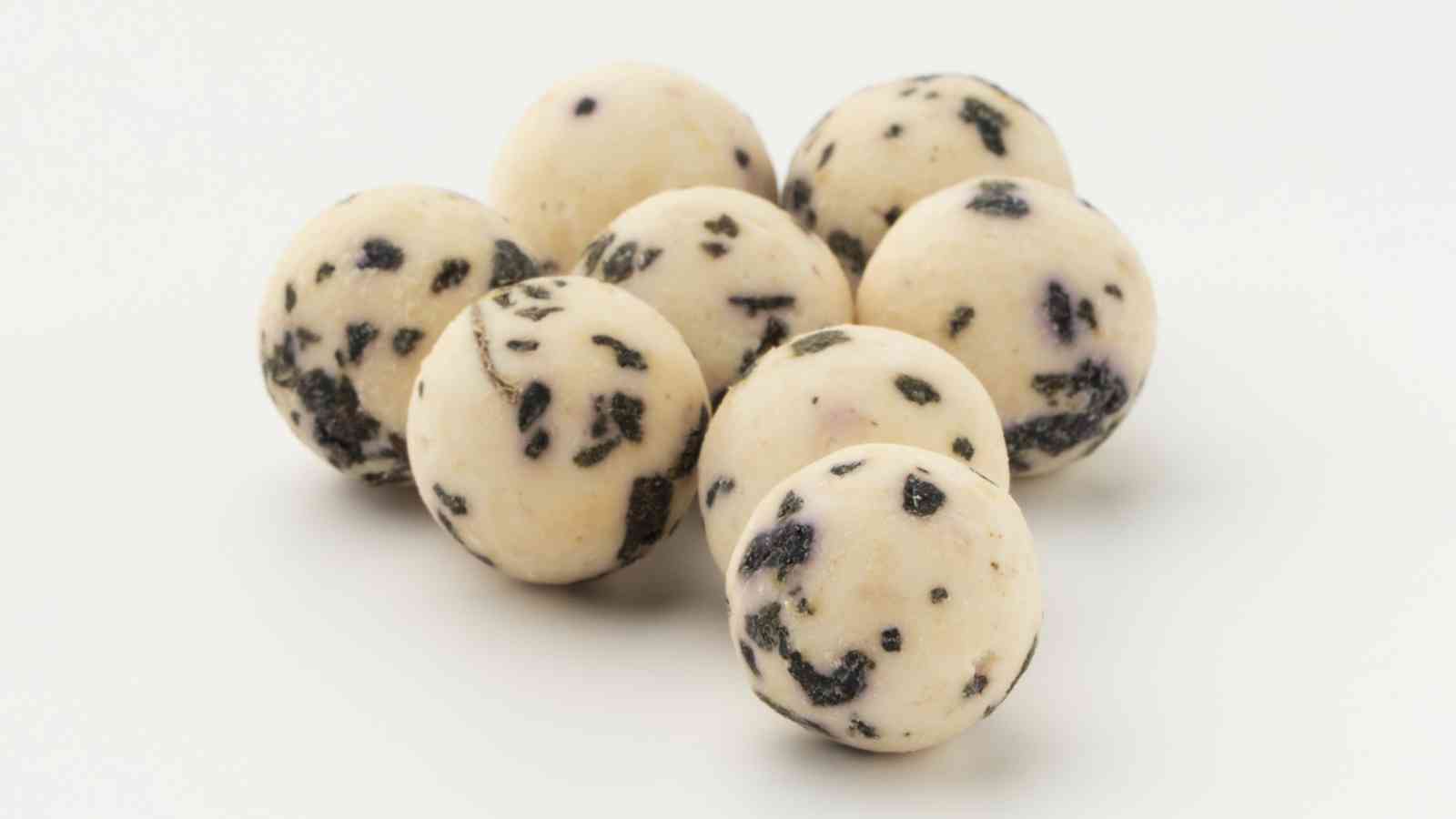 Eight round, white balls with dark specks are arranged closely together on a plain white background.