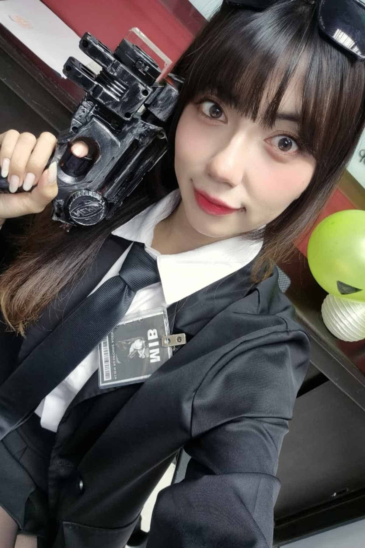 A woman in a suit poses for a selfie with a toy gun and a name badge labeled "MIB." A green balloon is visible in the background.