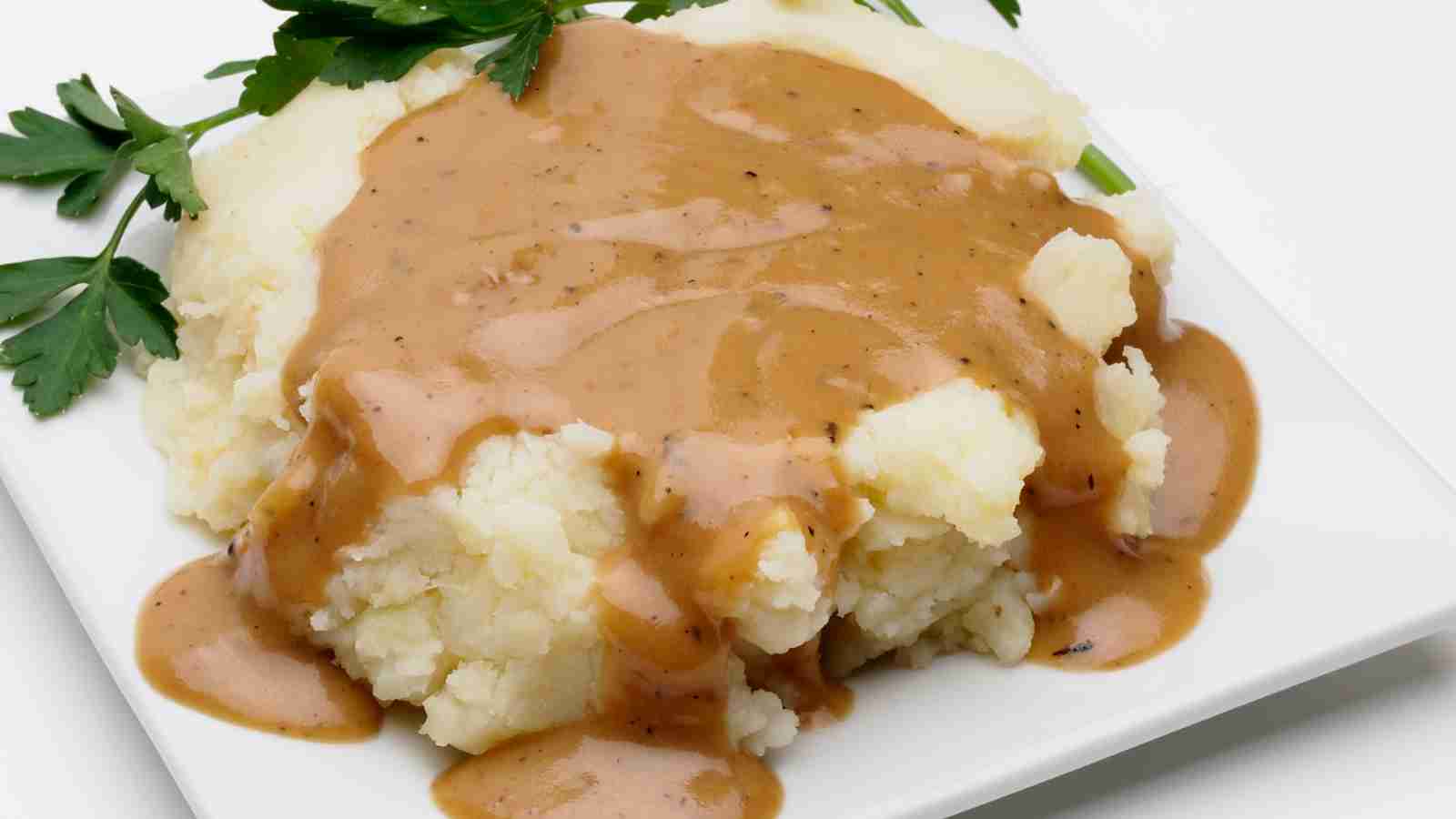 Mashed potatoes topped with brown gravy on a white plate, garnished with fresh parsley.
