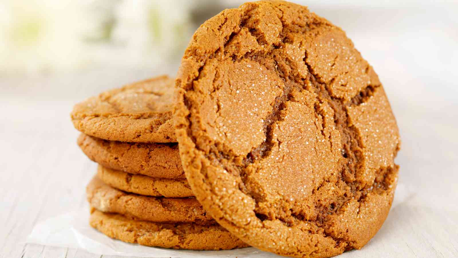 A stack of round, golden-brown cookies with a crackled surface sits on a light-colored surface.
