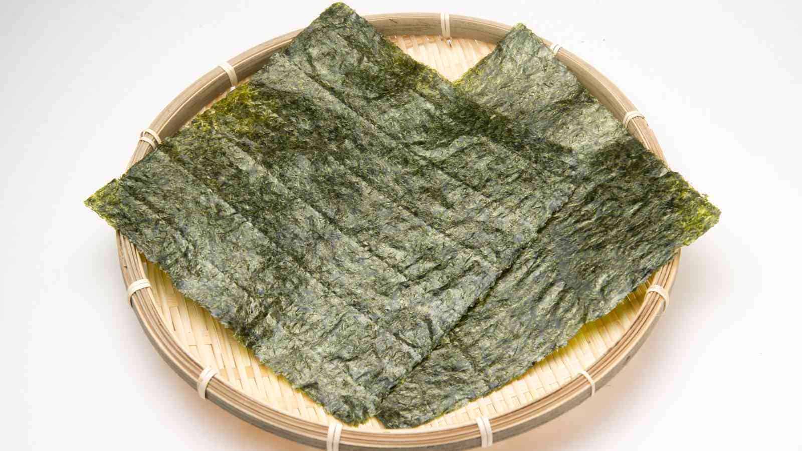 Two sheets of dried seaweed (nori) placed on a round bamboo tray against a white background.