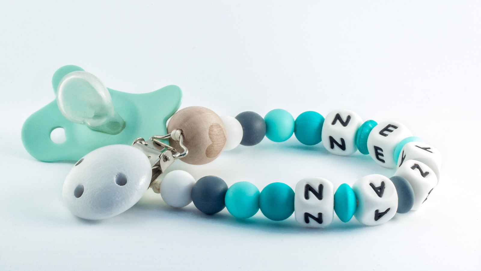 A mint green pacifier attached to a beaded clip with blue, white, and gray beads, including white cubes with black letters spelling “ENZAN.”.