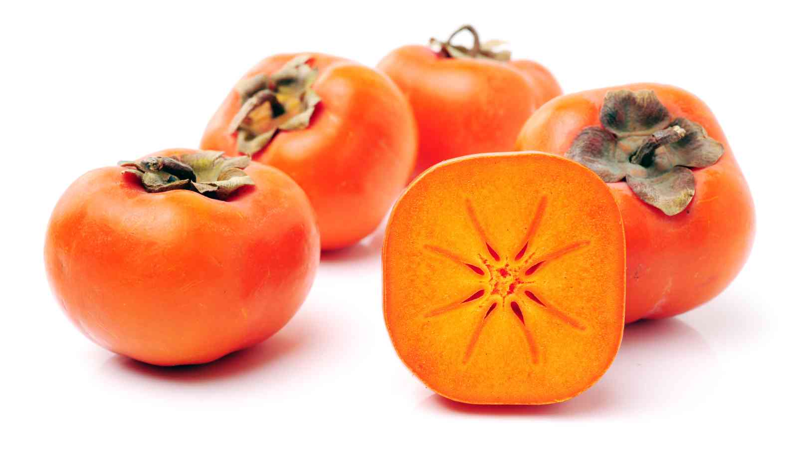 Four whole persimmons and one persimmon cut in half, showing the orange flesh and star-shaped pattern inside, on a white background.