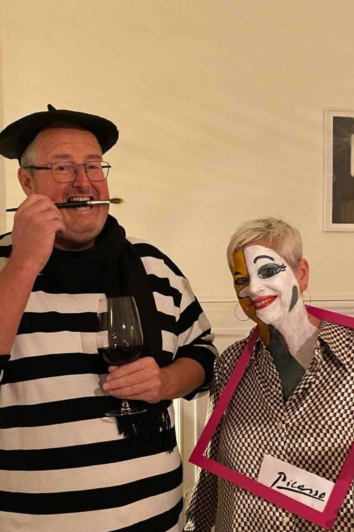 Two adults in costume: one dressed as a French artist with a beret, striped shirt, and paintbrush; the other with face paint and a pink frame labeled "Picasso."