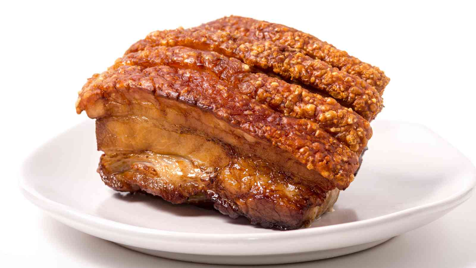 A piece of roasted pork belly with crispy crackling, served on a white plate against a white background.