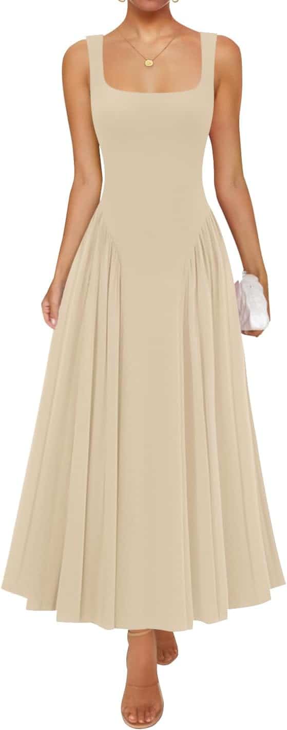 A woman wearing a sleeveless beige midi dress with a square neckline and flared skirt, holding a small white clutch, and wearing nude heels.