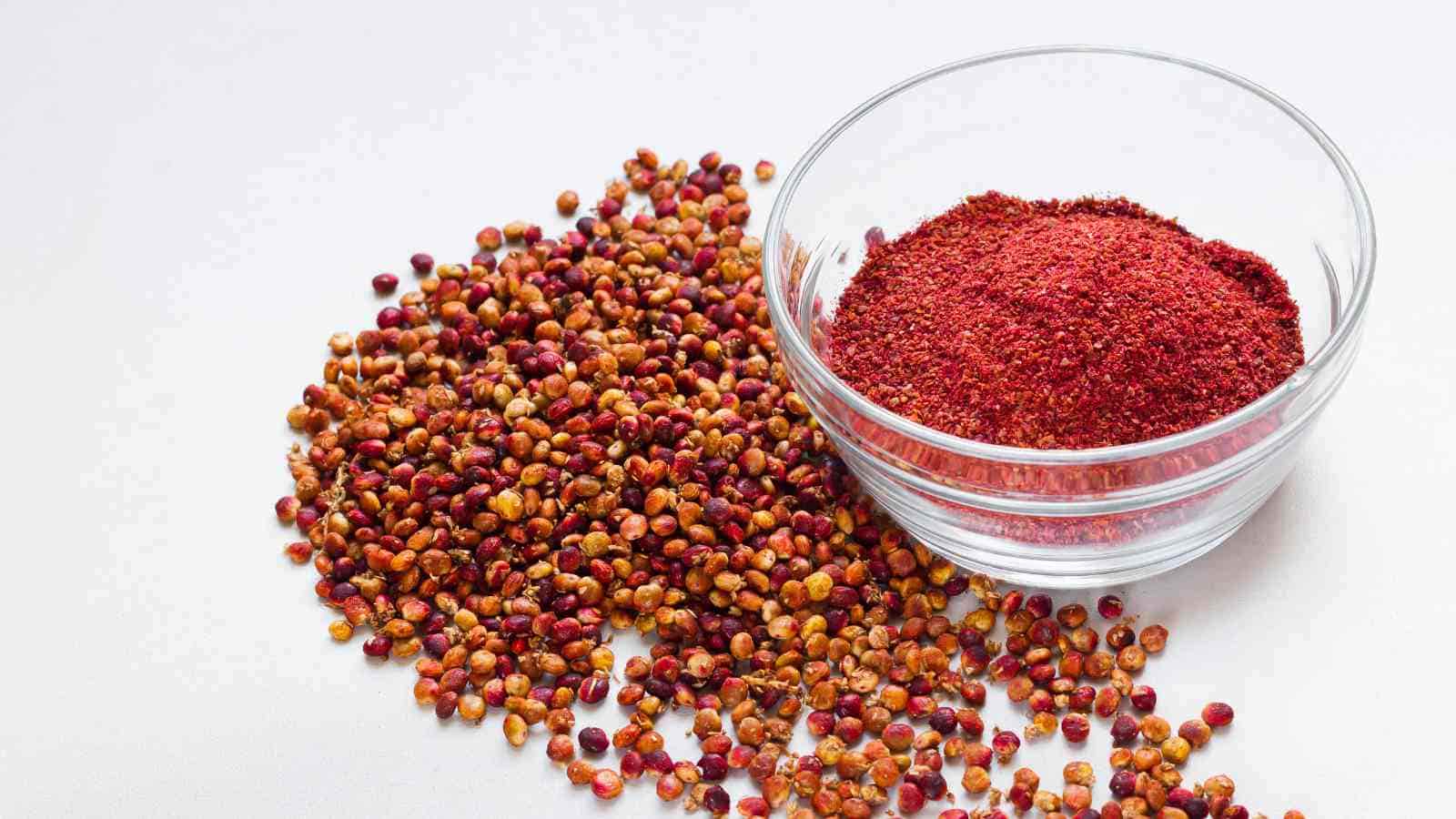 A glass bowl filled sumac on a white surface.