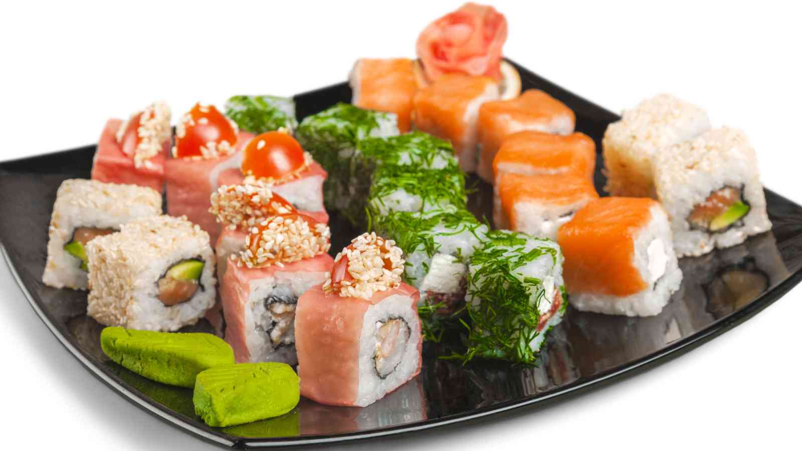 A black plate with assorted sushi rolls, including pieces topped with dill, sesame seeds, and fish, with wasabi and pickled ginger on the side.