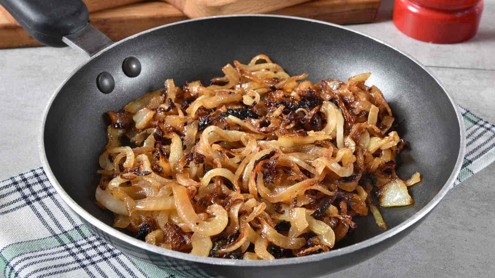 A frying pan filled with caramelized onions sits on a checkered kitchen towel on a countertop.