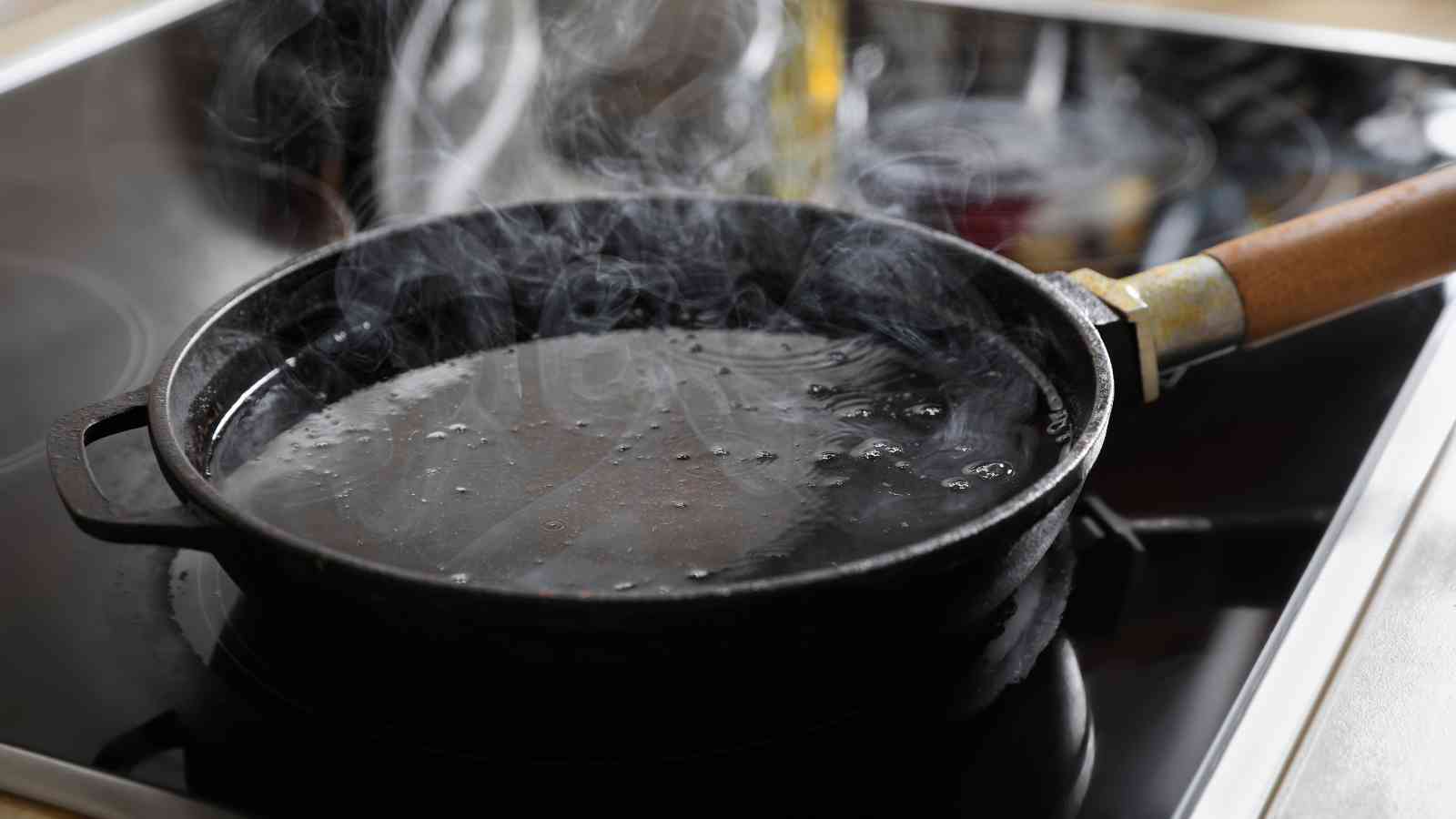 A black frying pan with hot oil is heating on an electric stovetop, with visible steam and bubbles rising from the surface.