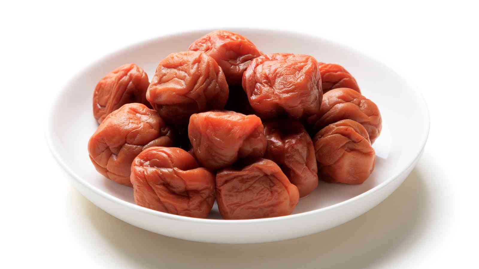 A white bowl filled with several pickled umeboshi plums on a white background.