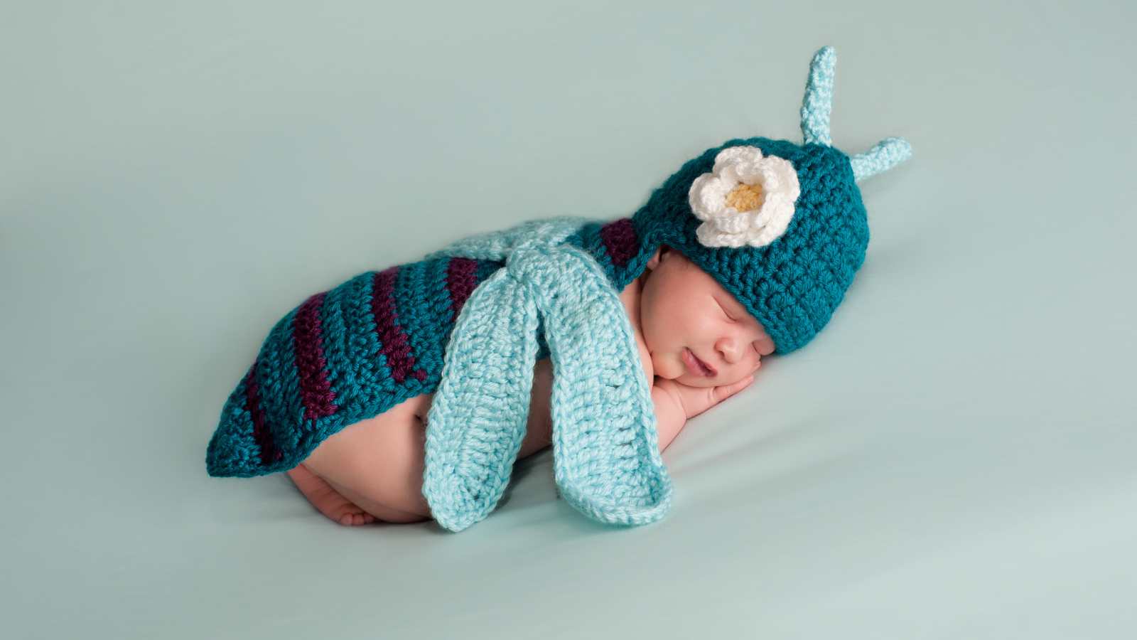 Baby lying on her back, wearing a knitted blue butterfly costume.