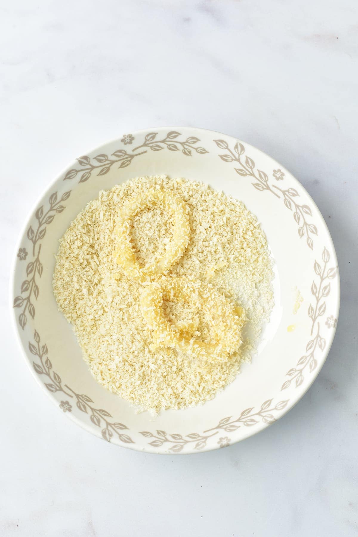 Two calamari rings coated in breadcrumbs, sitting in a bowl.