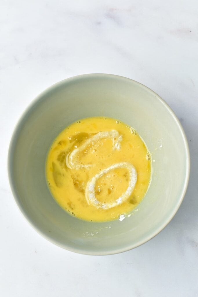 Two calamari rings soaked in beaten egg, sitting in a bowl.