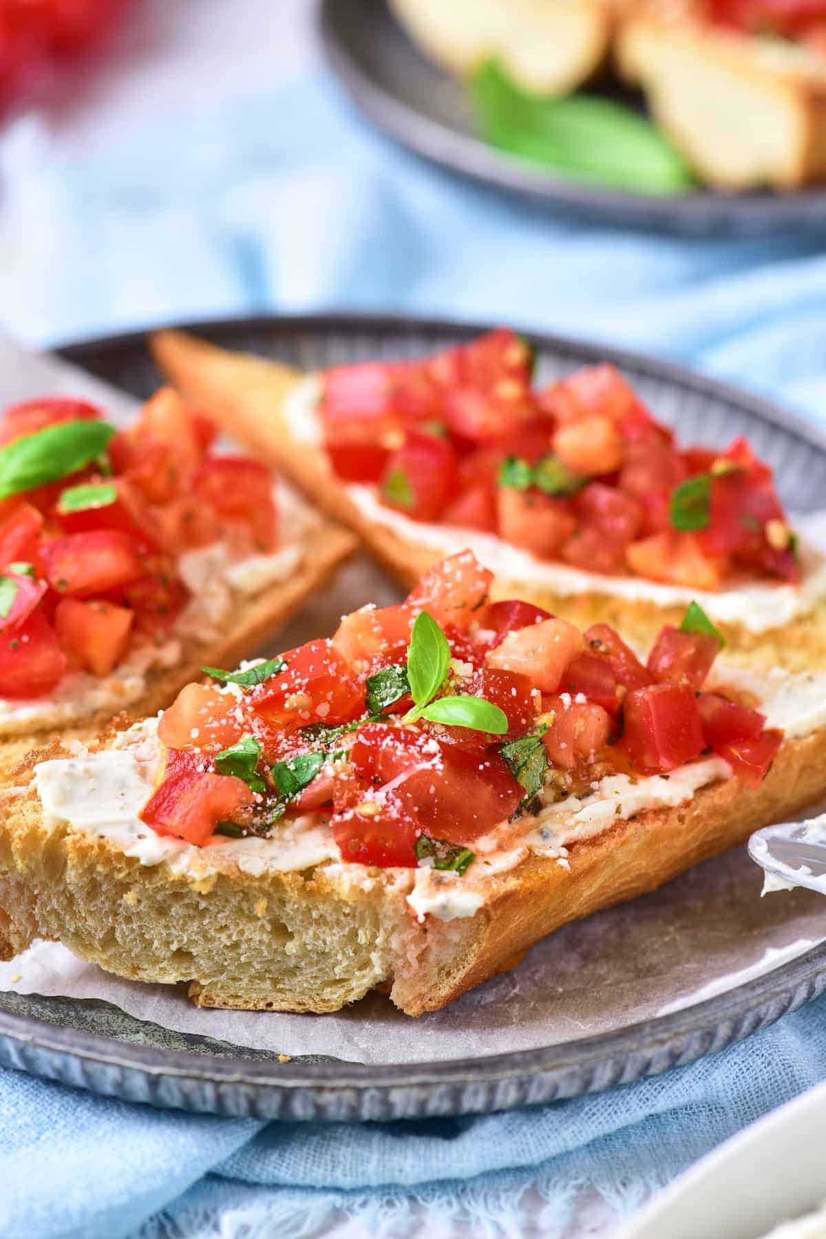Slices of toasted bread topped with diced tomatoes, herbs, and a layer of cheese spread are served on a round metal plate.