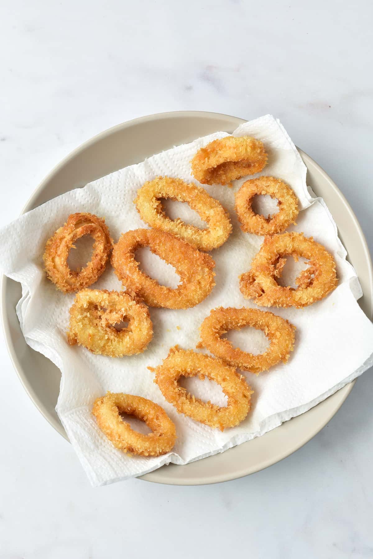 Cooked calamari rings placed on a tissue-lined plate.