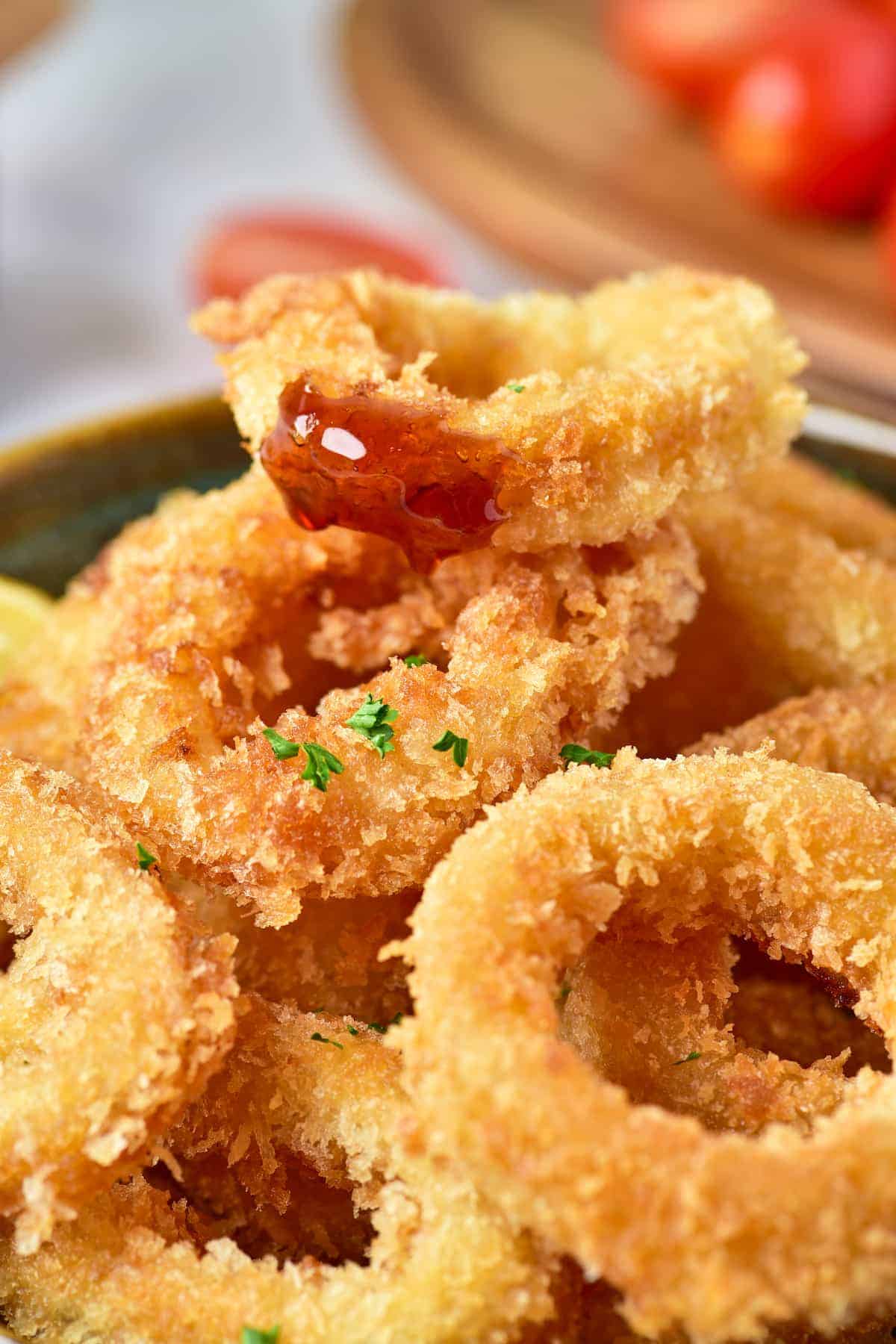 A focused shot of crispy calamari fries in a bowl with sliced lemons and a bit of sauce on one piece, all placed on a mat.