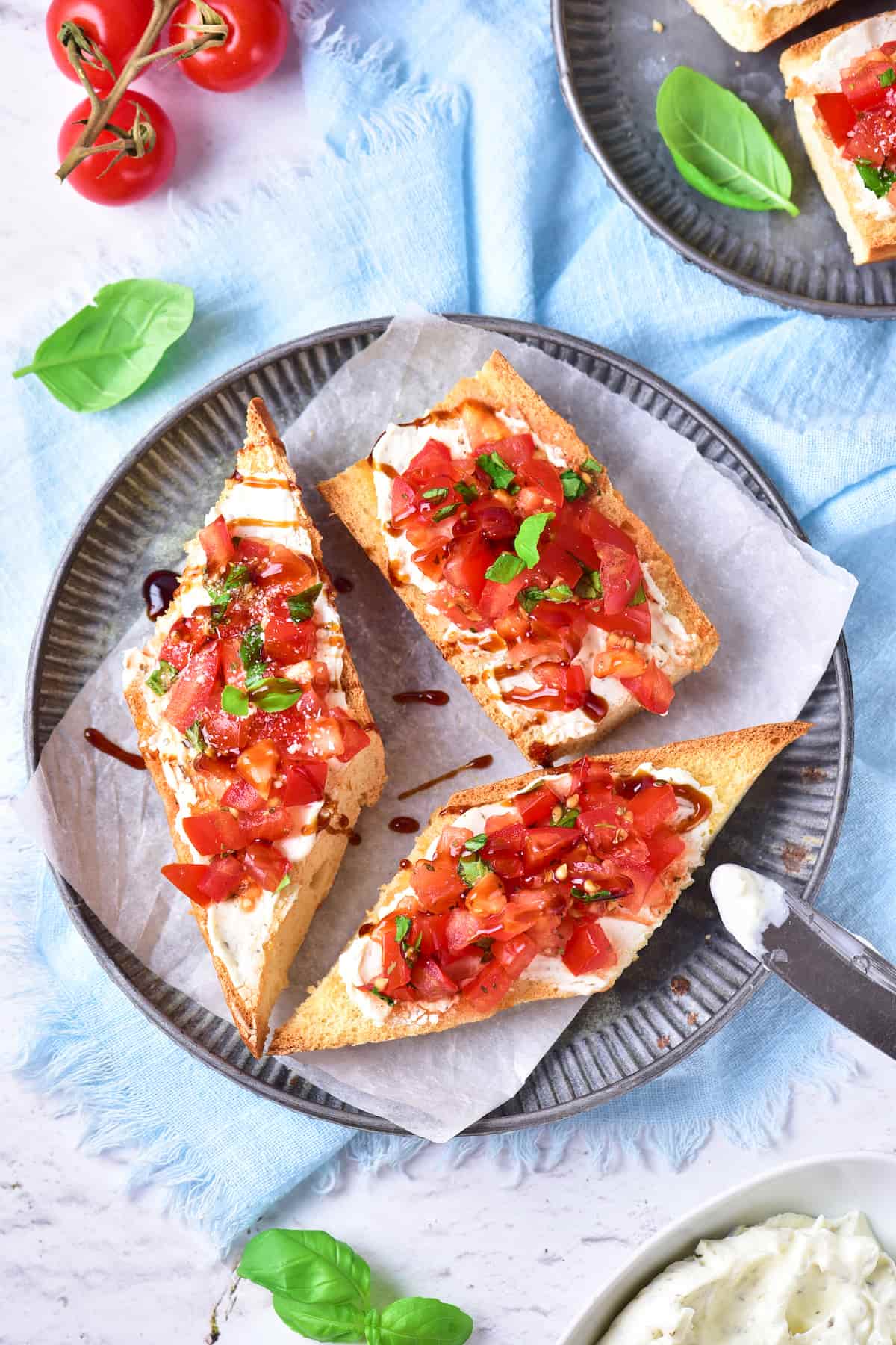 Two slices of toasted bread topped with diced tomatoes, herbs, and a drizzle of balsamic glaze on a gray plate, with a knife and fresh basil leaves nearby.