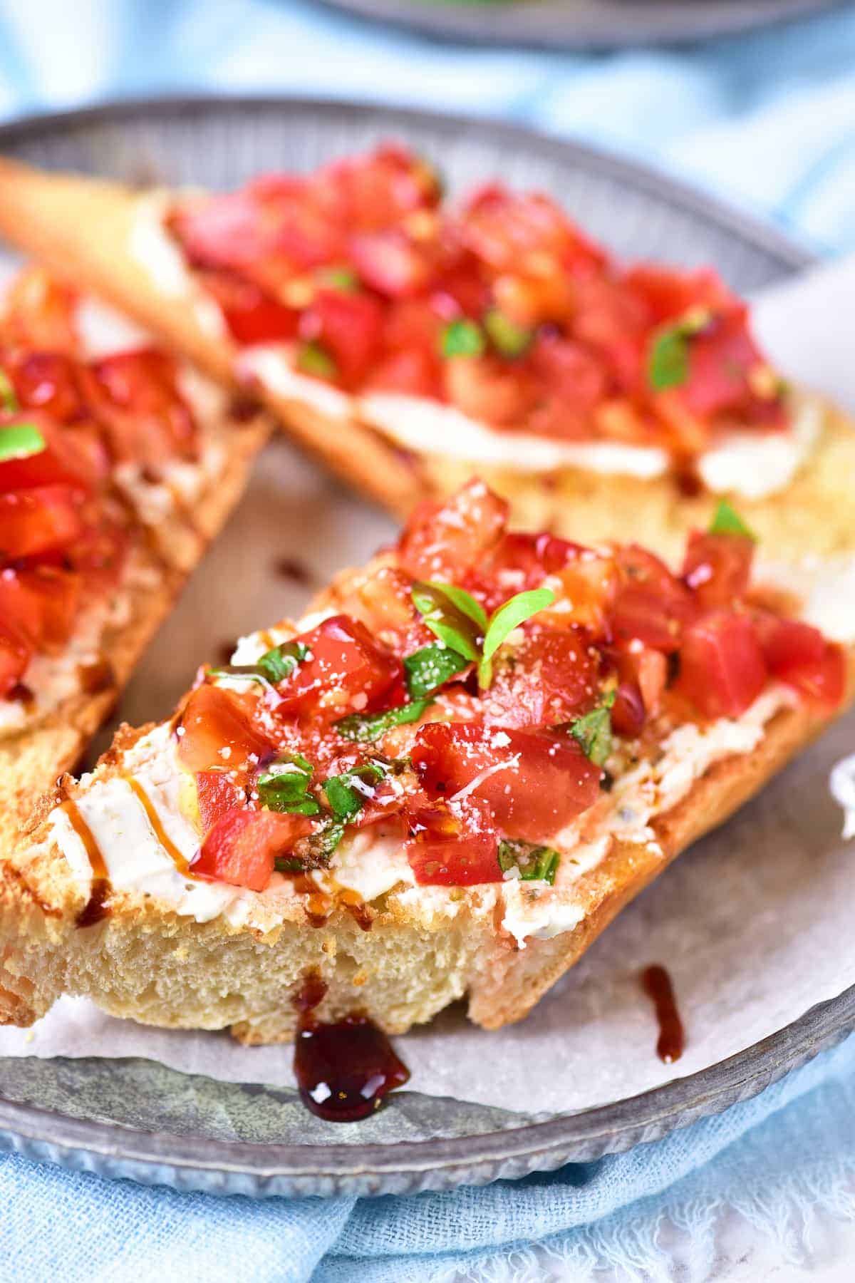 A slice of toasted bread topped with diced tomatoes, chopped herbs, creamy cheese, and a drizzle of balsamic glaze on a plate.
