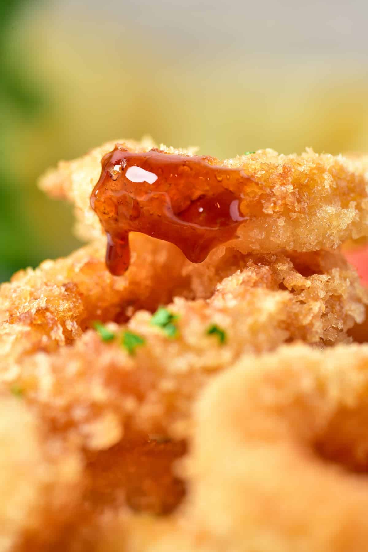 A zoomed-in shot of crispy calamari fries in a bowl, paired with sliced lemons and a hint of sauce on one piece of calamari, all set on a mat.