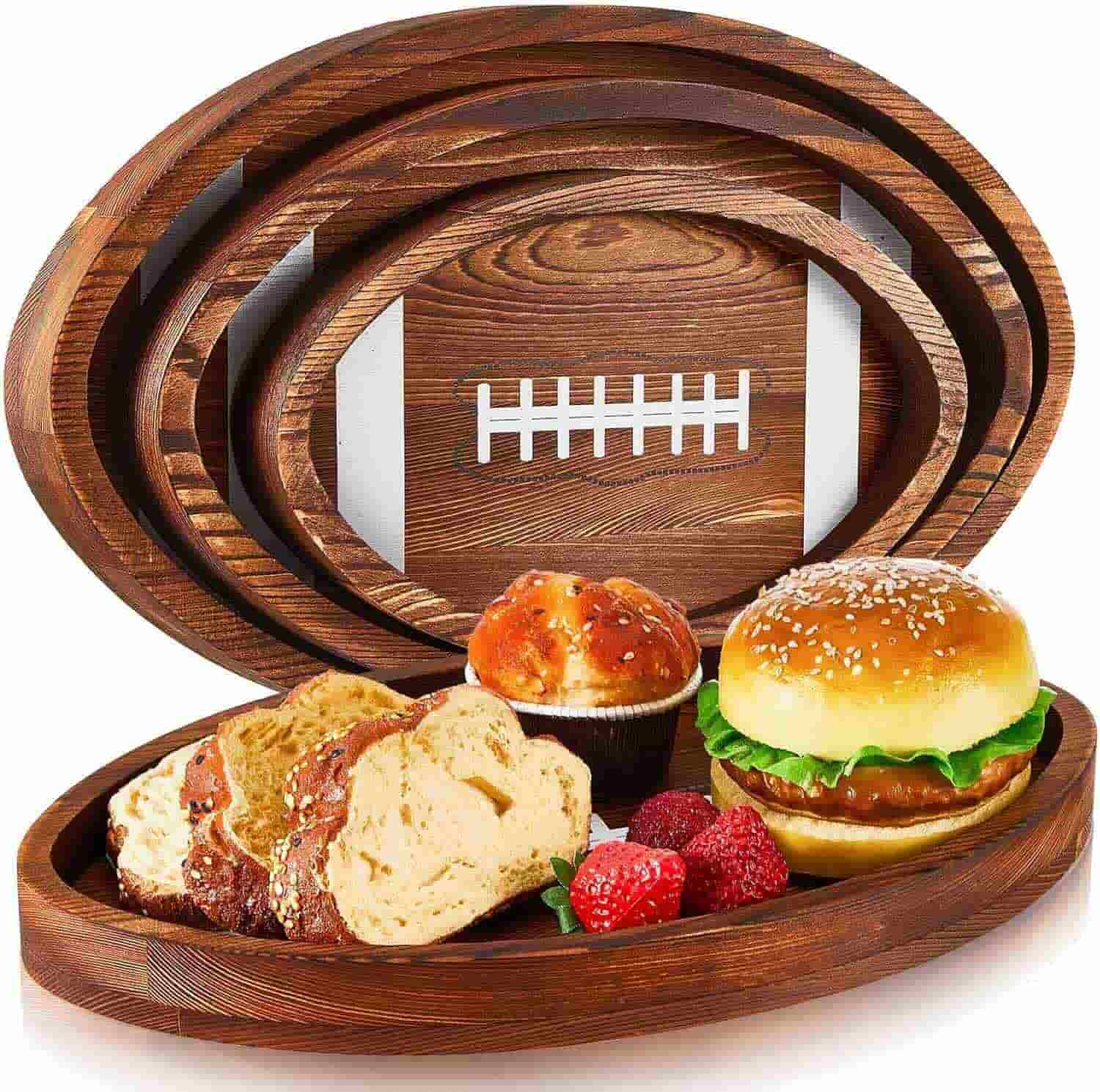 A wooden serving tray shaped like a football holds bread, a muffin, a sandwich with lettuce, and fresh berries.