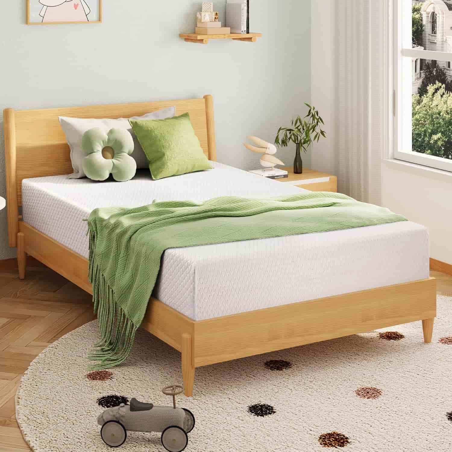 A neatly made bed with green and white bedding sits in a bright, modern bedroom with light wood furniture and a round rug.