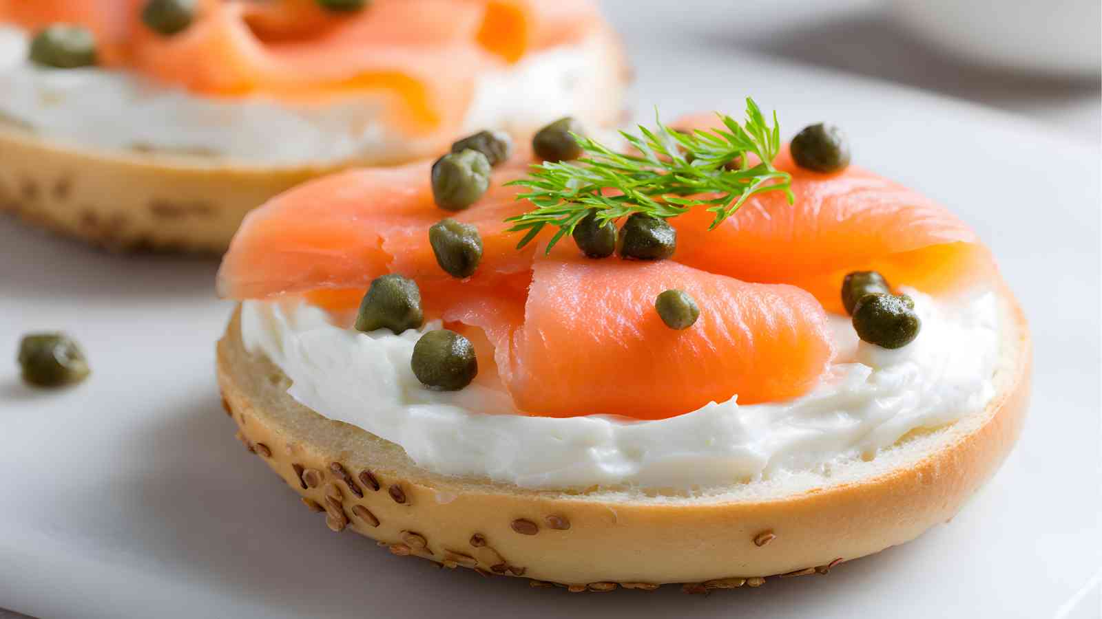 A sesame seed bagel half topped with cream cheese, slices of smoked salmon, capers, and a sprig of dill.