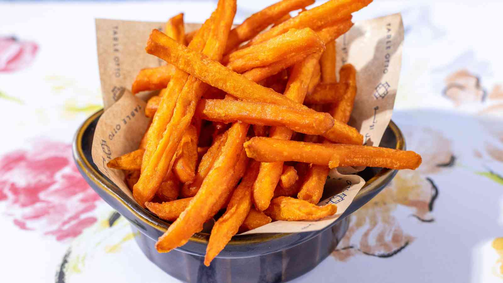 A bowl filled with crispy sweet potato fries placed on a sheet of brown parchment paper.