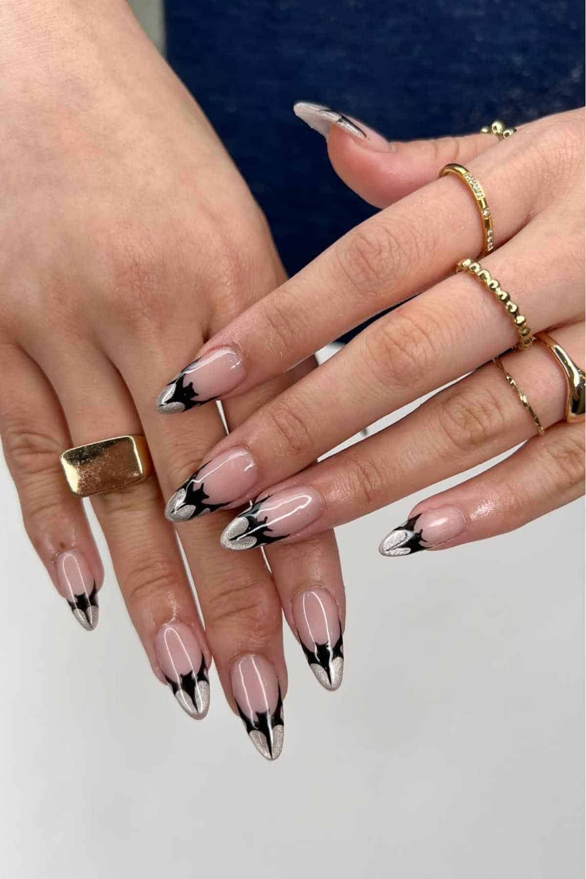 Hands with almond-shaped nails featuring a black and silver bat design on a nude base.