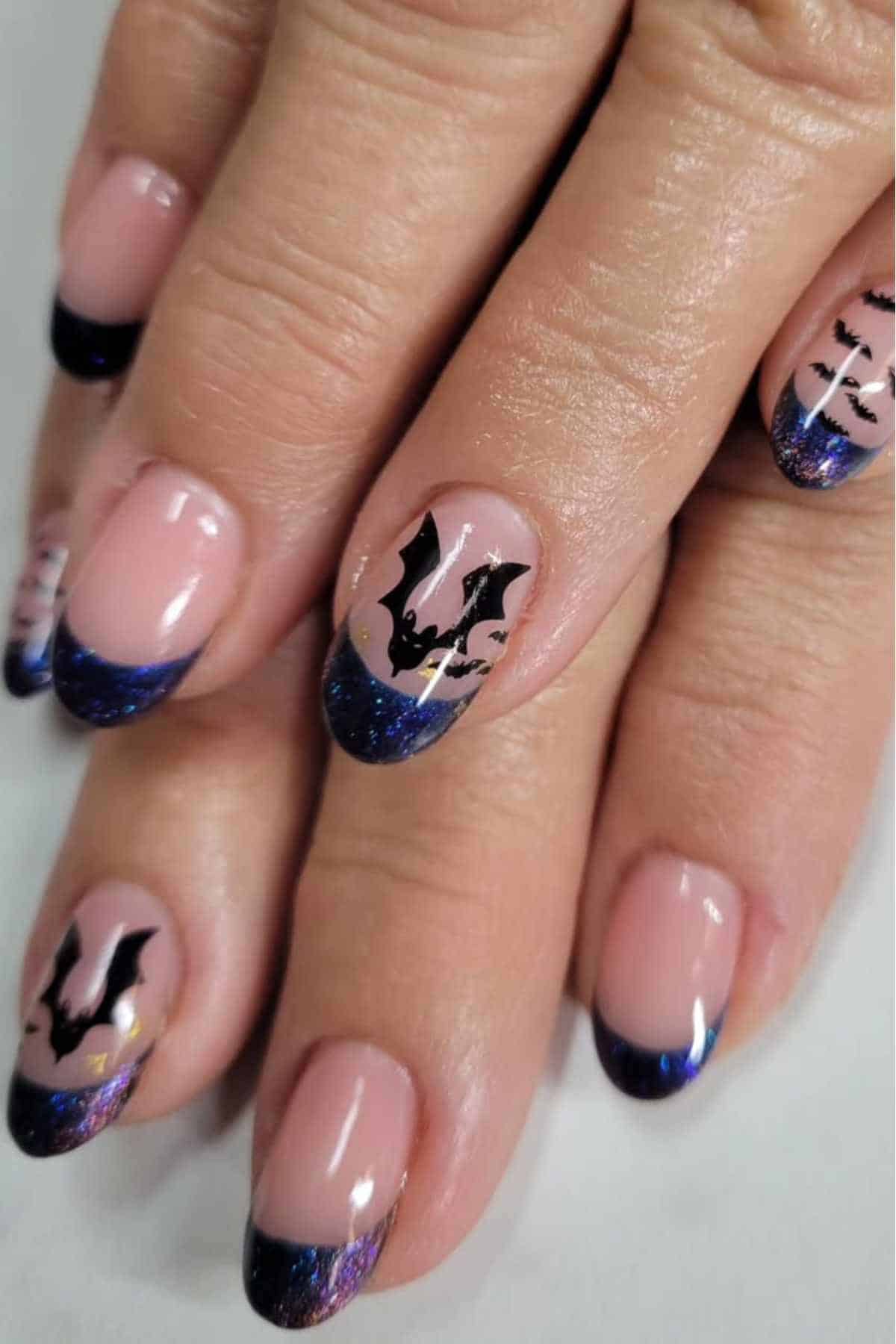 Close-up of a hand with a French manicure featuring dark blue glitter tips and black bat designs on some nails.