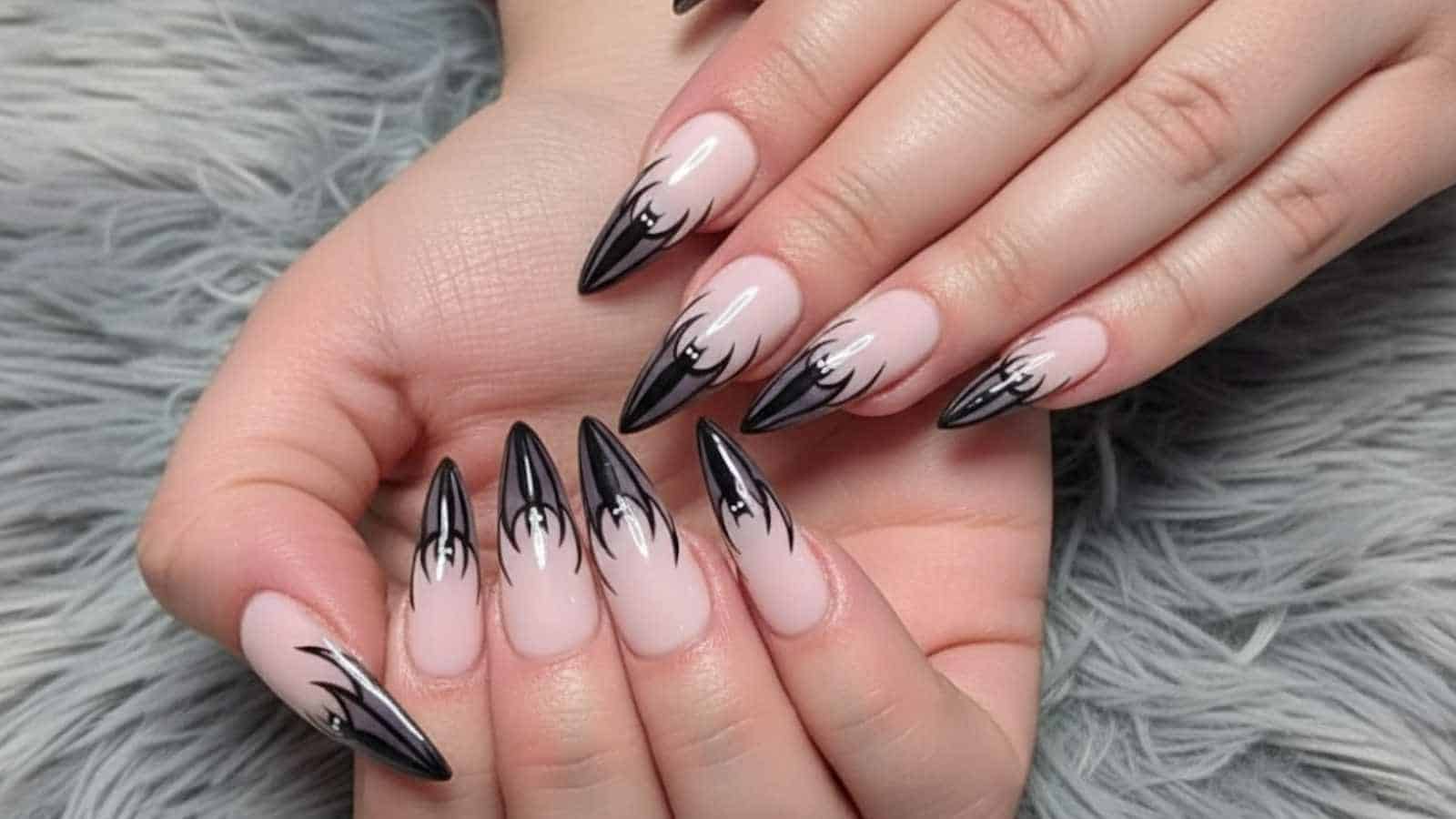 Hands with long, pointed nails featuring a black and white flame design over a nude base, resting on a gray textured surface—perfect for showcasing chic halloween bat nails inspiration.